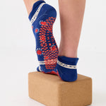 Woman on a yoga block wearing a full foot grip sock that has the design of a classic bandana, in a blue hue with red and white detailing. Made for pilates, barre, yoga and beyond. 