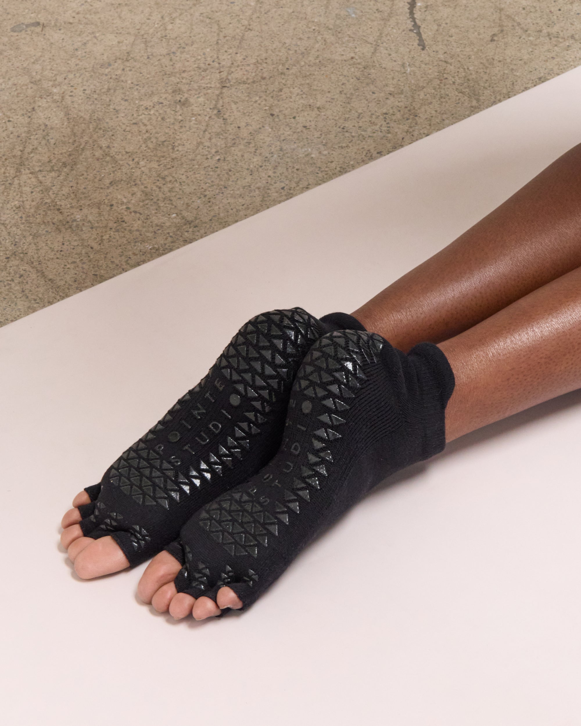 Women on a yoga mat wearing a solid black full foot 5 toeless grip socks, made for pilates, barre, yoga, and beyond.
