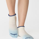 Women wearing an ombre white into light blue full foot grip sock with a navy blue ruffle cuff and inhale and exhale written on the top of the toes, made for pilates, barre, yoga, and beyond.