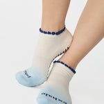Women wearing an ombre white into light blue full foot grip sock with a navy blue ruffle cuff and inhale and exhale written on the top of the toes, made for pilates, barre, yoga, and beyond.