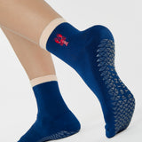 Woman wearing a solid navy blue ankle grip sock with a beige solid cuff and a red lobster embroidered on the ankle. Made for pilates, barre, yoga, and beyond. 