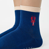 Woman wearing a solid navy blue ankle grip sock with a beige solid cuff and a red lobster embroidered on the ankle. Made for pilates, barre, yoga, and beyond. 