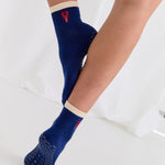 Woman wearing a solid navy blue ankle grip sock with a beige solid cuff and a red lobster embroidered on the ankle. Made for pilates, barre, yoga, and beyond. 