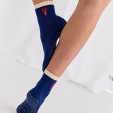 Woman wearing a solid navy blue ankle grip sock with a beige solid cuff and a red lobster embroidered on the ankle. Made for pilates, barre, yoga, and beyond. 
