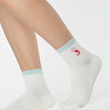 Woman wearing a solid white ankle grip sock with a light blue solid cuff and a red shrimp embroidered on the ankle. Made for pilates, barre, yoga, and beyond. 