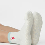 Woman wearing a solid white ankle grip sock with a light blue solid cuff and a red shrimp embroidered on the ankle. Made for pilates, barre, yoga, and beyond. 
