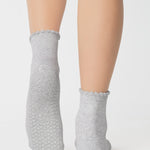 Women wearing a solid heather grey ankle grip sock with a ruffle cuff and with a red cherry on the top of the toes, made for pilates, barre, yoga, and beyond.