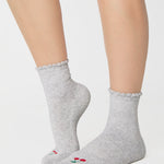 Women wearing a solid heather grey ankle grip sock with a ruffle cuff and with a red cherry on the top of the toes, made for pilates, barre, yoga, and beyond.