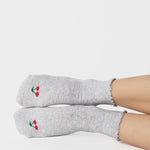 Women wearing a solid heather grey ankle grip sock with a ruffle cuff and with a red cherry on the top of the toes, made for pilates, barre, yoga, and beyond.