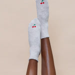 Women wearing a solid heather grey ankle grip sock with a ruffle cuff and with a red cherry on the top of the toes, made for pilates, barre, yoga, and beyond.