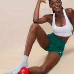 Women wearing a solid heather grey ankle grip sock with a ruffle cuff and with a red cherry on the top of the toes, made for pilates, barre, yoga, and beyond.