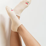 Women wearing a solid off white ivory full foot grip sock with a ruffle cuff and with a red cherry on the top of the toes, made for pilates, barre, yoga, and beyond.