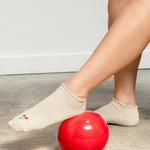 Women wearing a solid off white ivory full foot grip sock with a ruffle cuff and with a red cherry on the top of the toes, made for pilates, barre, yoga, and beyond.