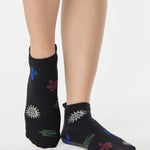 Woman wearing a black full foot grip sock with woven suns, cacti, and snakes. Made for pilates, barre, yoga, and beyond. 