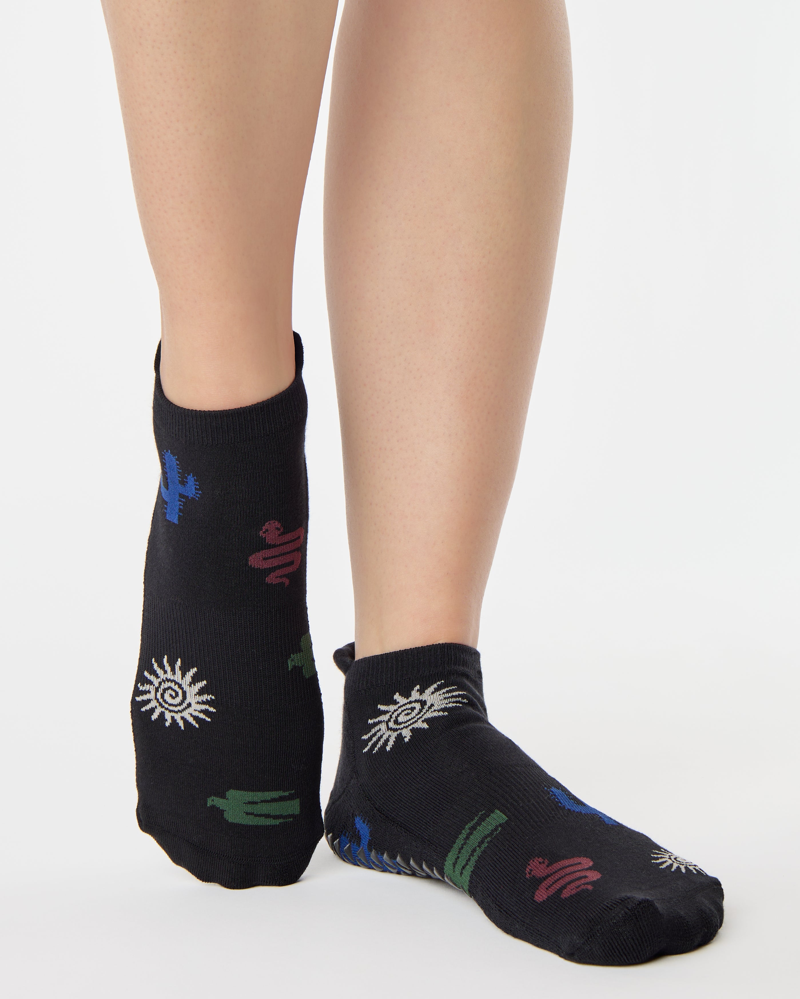 Woman wearing a black full foot grip sock with woven suns, cacti, and snakes. Made for pilates, barre, yoga, and beyond. 