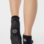 Woman wearing a black full foot grip sock with woven suns, cacti, and snakes. Made for pilates, barre, yoga, and beyond. 