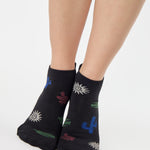 Woman wearing a black full foot grip sock with woven suns, cacti, and snakes. Made for pilates, barre, yoga, and beyond. 