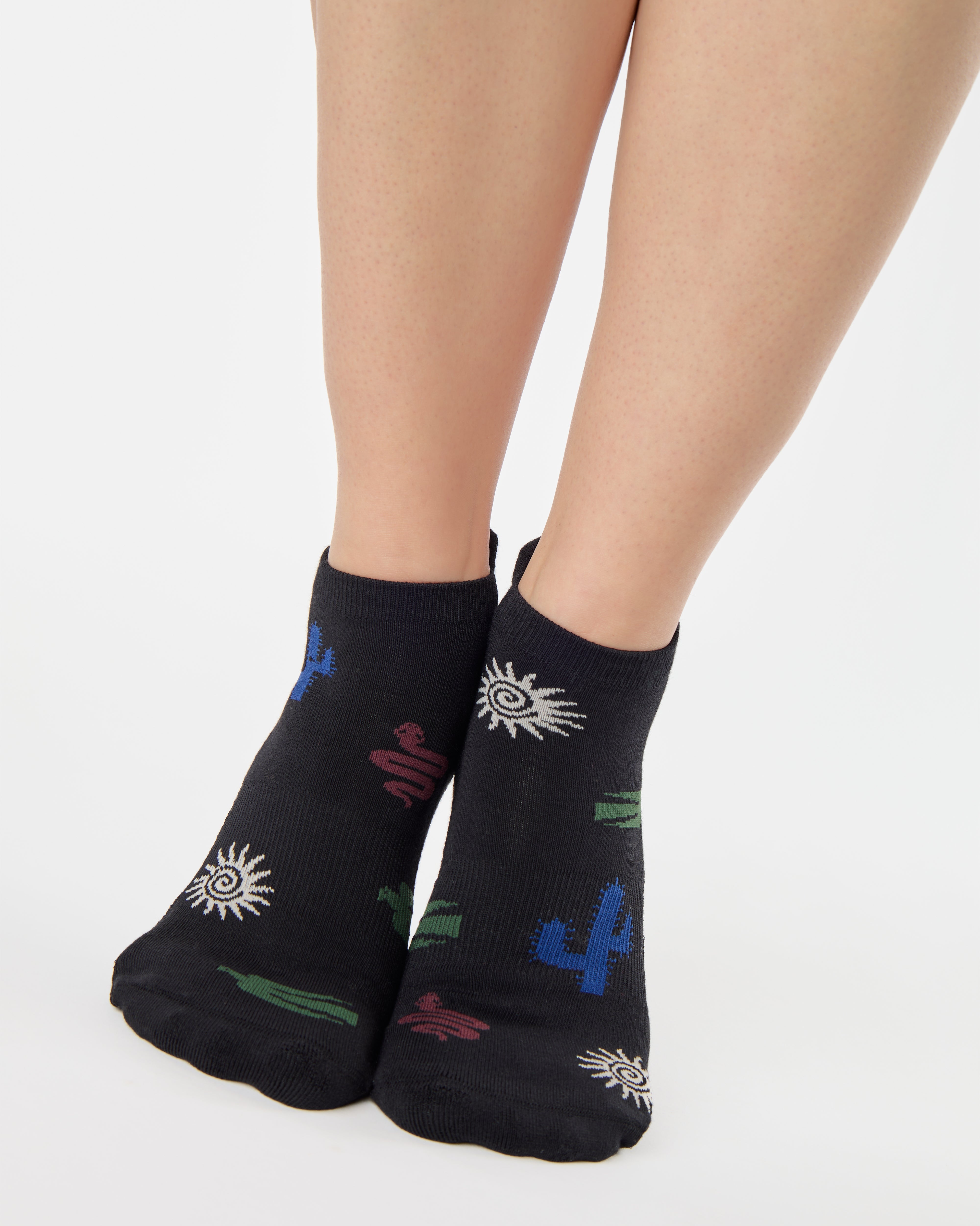 Woman wearing a black full foot grip sock with woven suns, cacti, and snakes. Made for pilates, barre, yoga, and beyond. 
