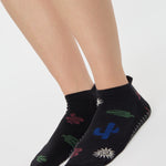 Woman wearing a black full foot grip sock with woven suns, cacti, and snakes. Made for pilates, barre, yoga, and beyond. 