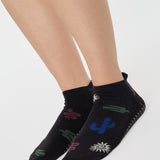 Woman wearing a black full foot grip sock with woven suns, cacti, and snakes. Made for pilates, barre, yoga, and beyond. 