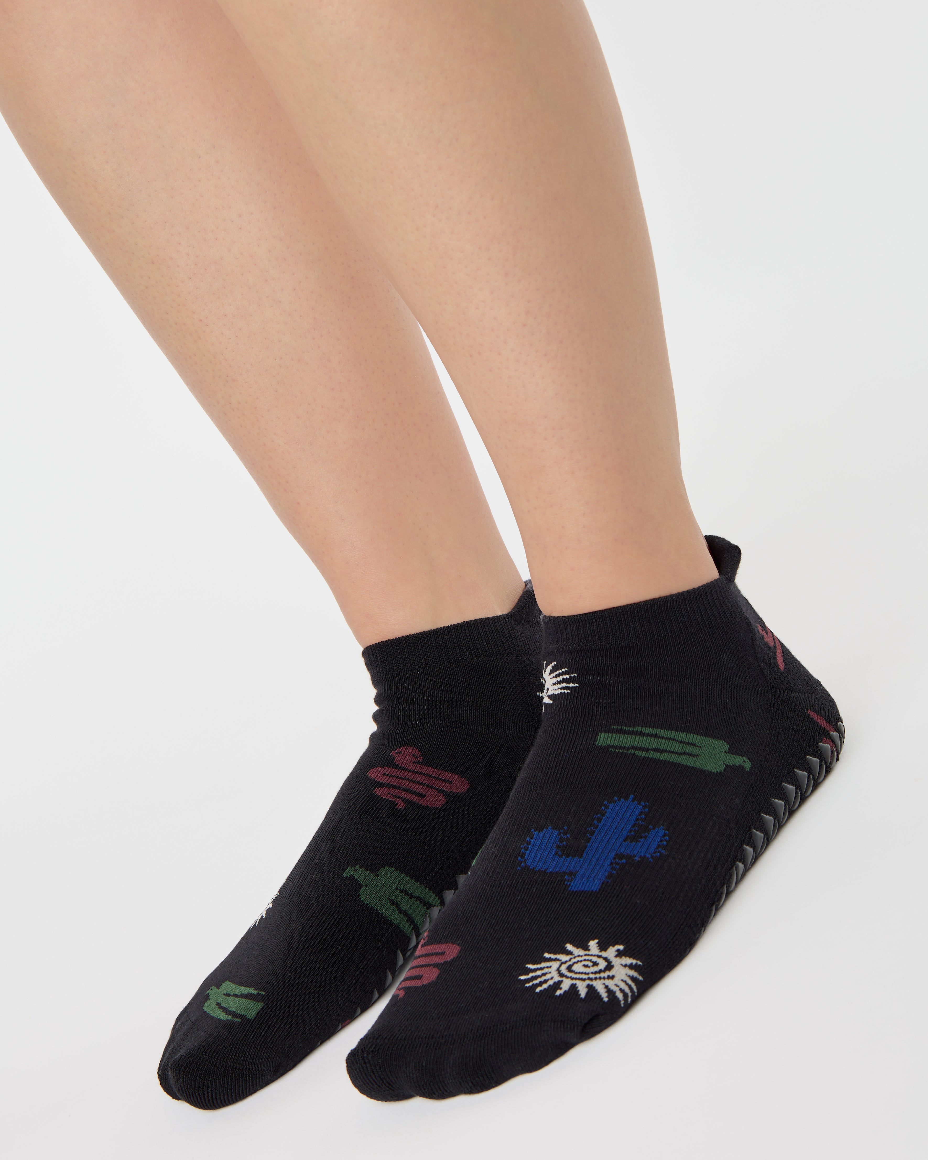 Woman wearing a black full foot grip sock with woven suns, cacti, and snakes. Made for pilates, barre, yoga, and beyond. 