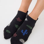 Woman wearing a black full foot grip sock with woven suns, cacti, and snakes. Made for pilates, barre, yoga, and beyond. 