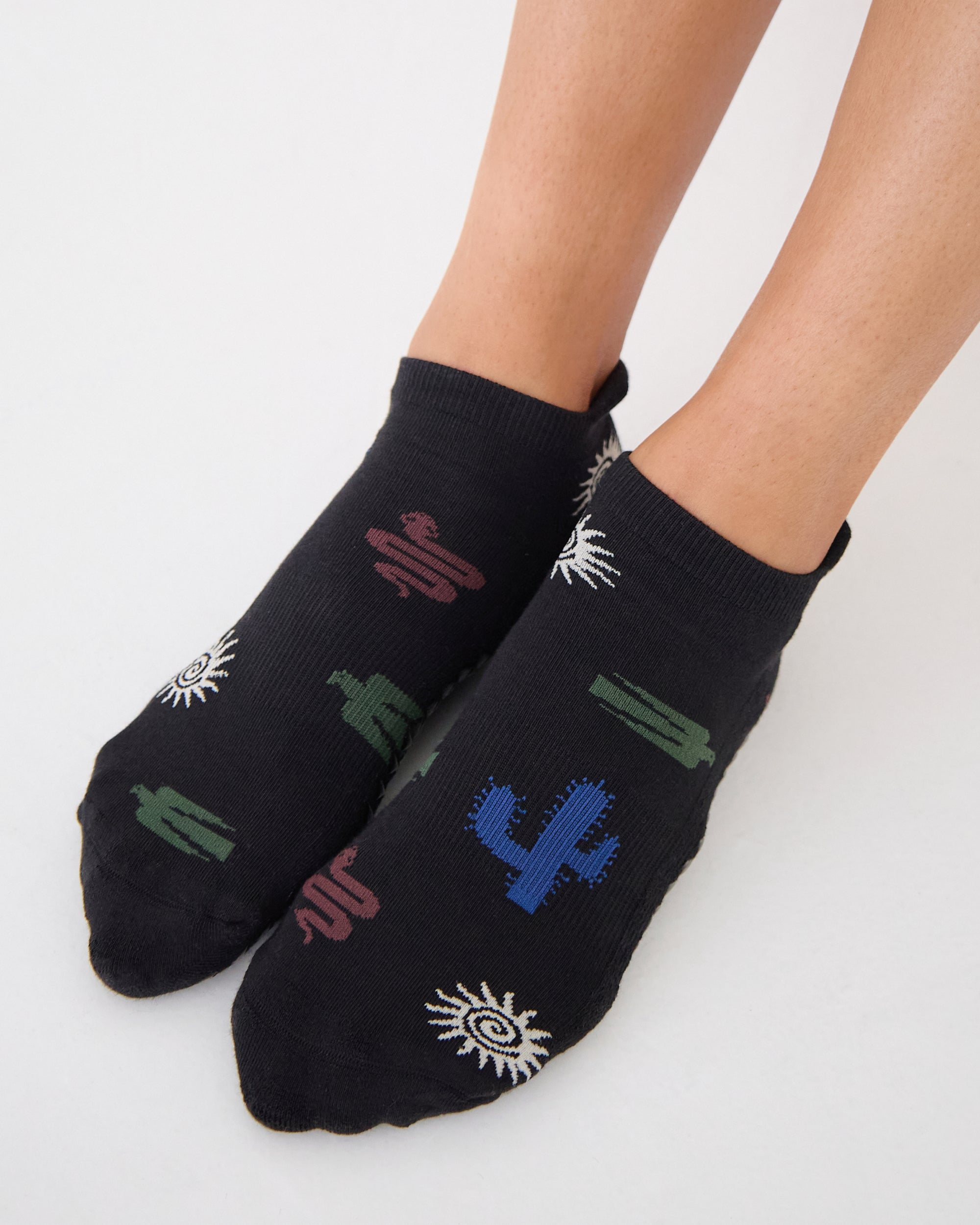 Woman wearing a black full foot grip sock with woven suns, cacti, and snakes. Made for pilates, barre, yoga, and beyond. 