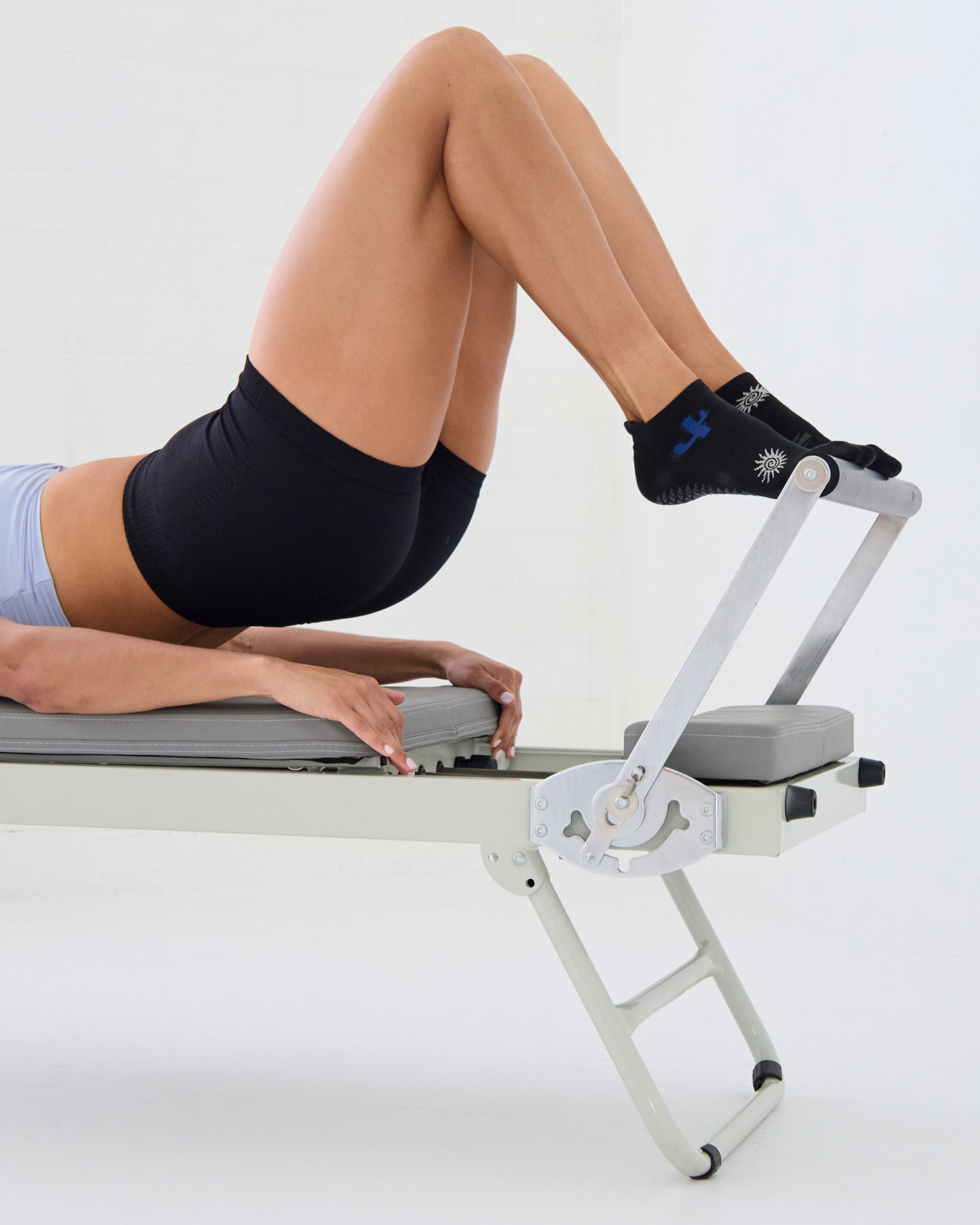 Woman on a reformer wearing a black full foot grip sock with woven suns, cacti, and snakes. Made for pilates, barre, yoga, and beyond. 
