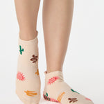 Woman wearing a beige full foot grip sock with woven suns, cacti, and snakes. Made for pilates, barre, yoga, and beyond. 