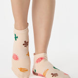 Woman wearing a beige full foot grip sock with woven suns, cacti, and snakes. Made for pilates, barre, yoga, and beyond. 