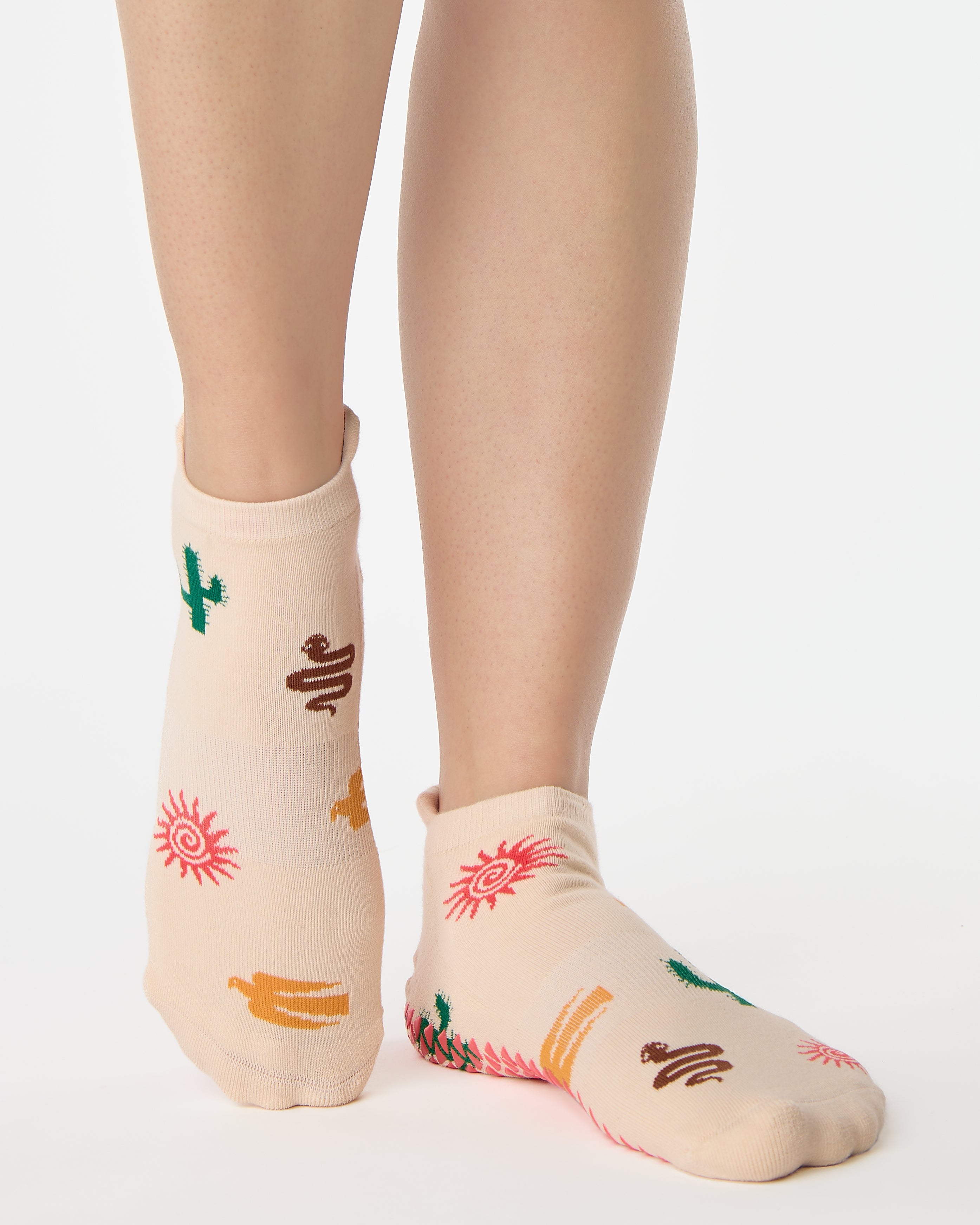 Woman wearing a beige full foot grip sock with woven suns, cacti, and snakes. Made for pilates, barre, yoga, and beyond. 