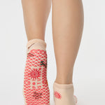 Woman wearing a beige full foot grip sock with woven suns, cacti, and snakes. Made for pilates, barre, yoga, and beyond. 