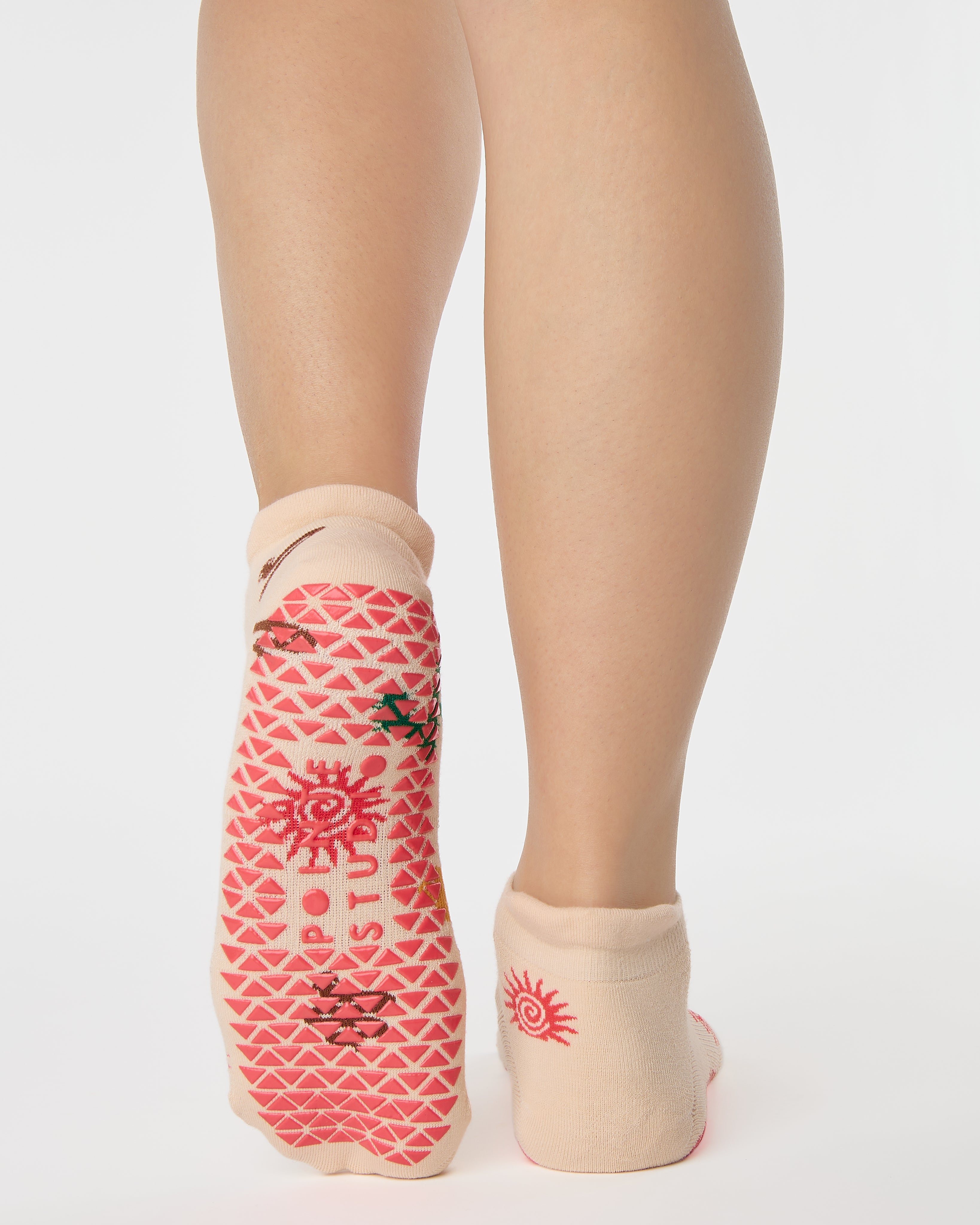 Woman wearing a beige full foot grip sock with woven suns, cacti, and snakes. Made for pilates, barre, yoga, and beyond. 