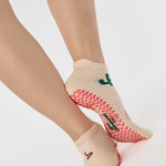 Woman wearing a beige full foot grip sock with woven suns, cacti, and snakes. Made for pilates, barre, yoga, and beyond. 