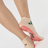Woman wearing a beige full foot grip sock with woven suns, cacti, and snakes. Made for pilates, barre, yoga, and beyond. 