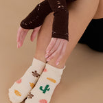 Woman wearing a beige full foot grip sock with woven suns, cacti, and snakes. Made for pilates, barre, yoga, and beyond. 