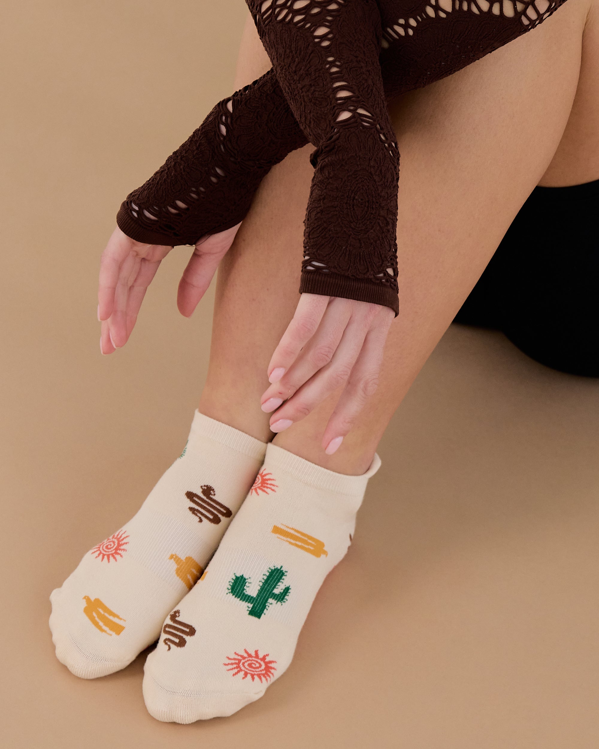 Woman wearing a beige full foot grip sock with woven suns, cacti, and snakes. Made for pilates, barre, yoga, and beyond. 