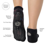 Woman wearing a black full foot grip sock with woven suns, cacti, and snakes. Made for pilates, barre, yoga, and beyond. With the product features listed. 