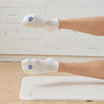 Women on a yoga mat wearing a solid white full foot grip sock with a blue evil eye motiff on the top of the toes, made for pilates, barre, yoga, and beyond.
