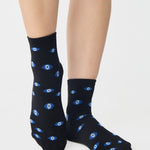 Women wearing a black ankle grip sock with evil eye pattern all around, made for pilates, barre, yoga, and beyond.