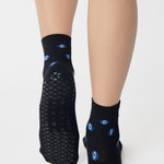 Women wearing a black ankle grip sock with evil eye pattern all around, made for pilates, barre, yoga, and beyond.