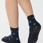 Women wearing a black ankle grip sock with evil eye pattern all around, made for pilates, barre, yoga, and beyond.