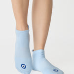 Women wearing a solid white full foot grip sock with a blue evil eye motiff on the top of the toes, made for pilates, barre, yoga, and beyond.