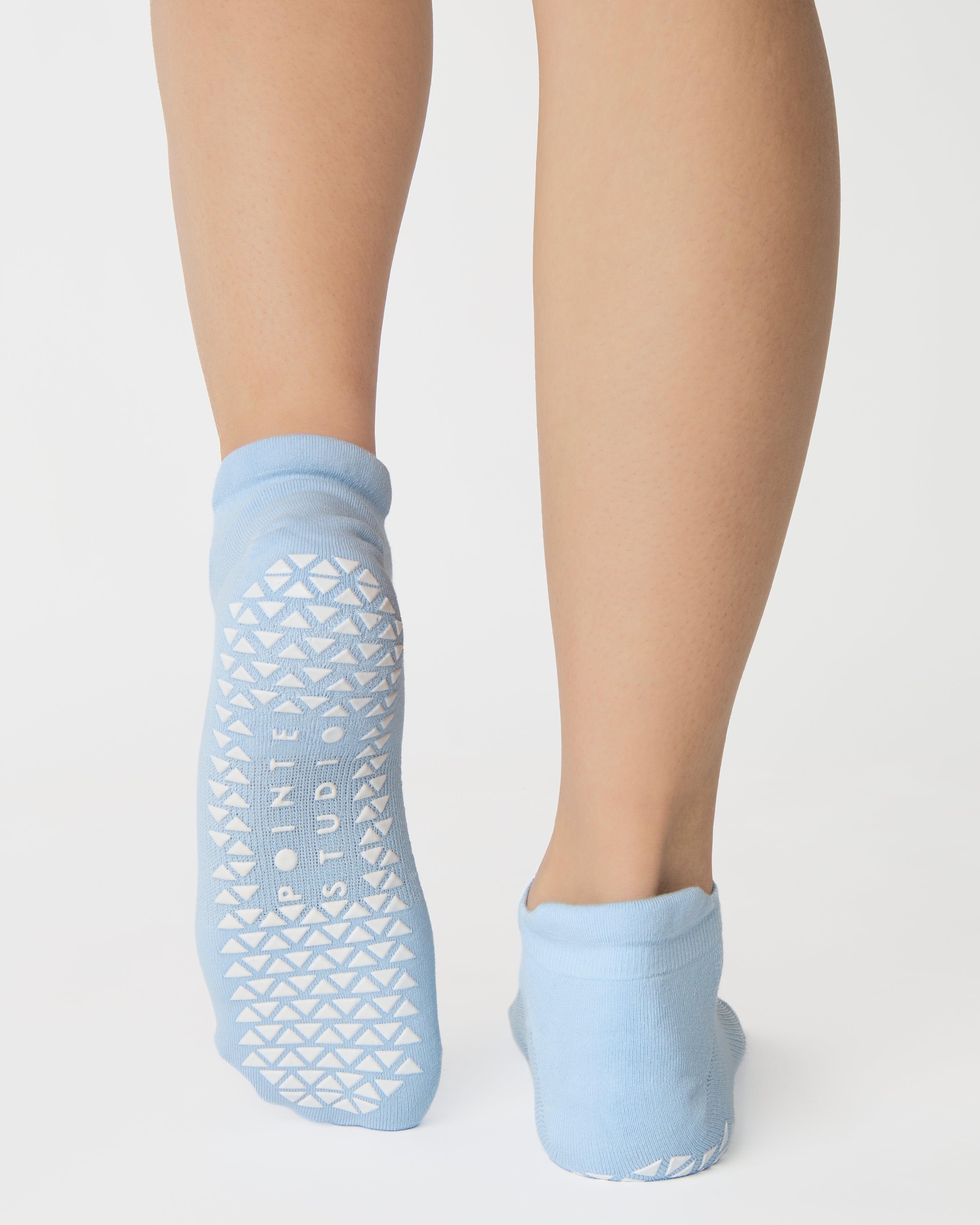 Women wearing a solid white full foot grip sock with a blue evil eye motiff on the top of the toes, made for pilates, barre, yoga, and beyond.