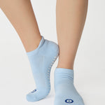 Women wearing a solid white full foot grip sock with a blue evil eye motiff on the top of the toes, made for pilates, barre, yoga, and beyond.