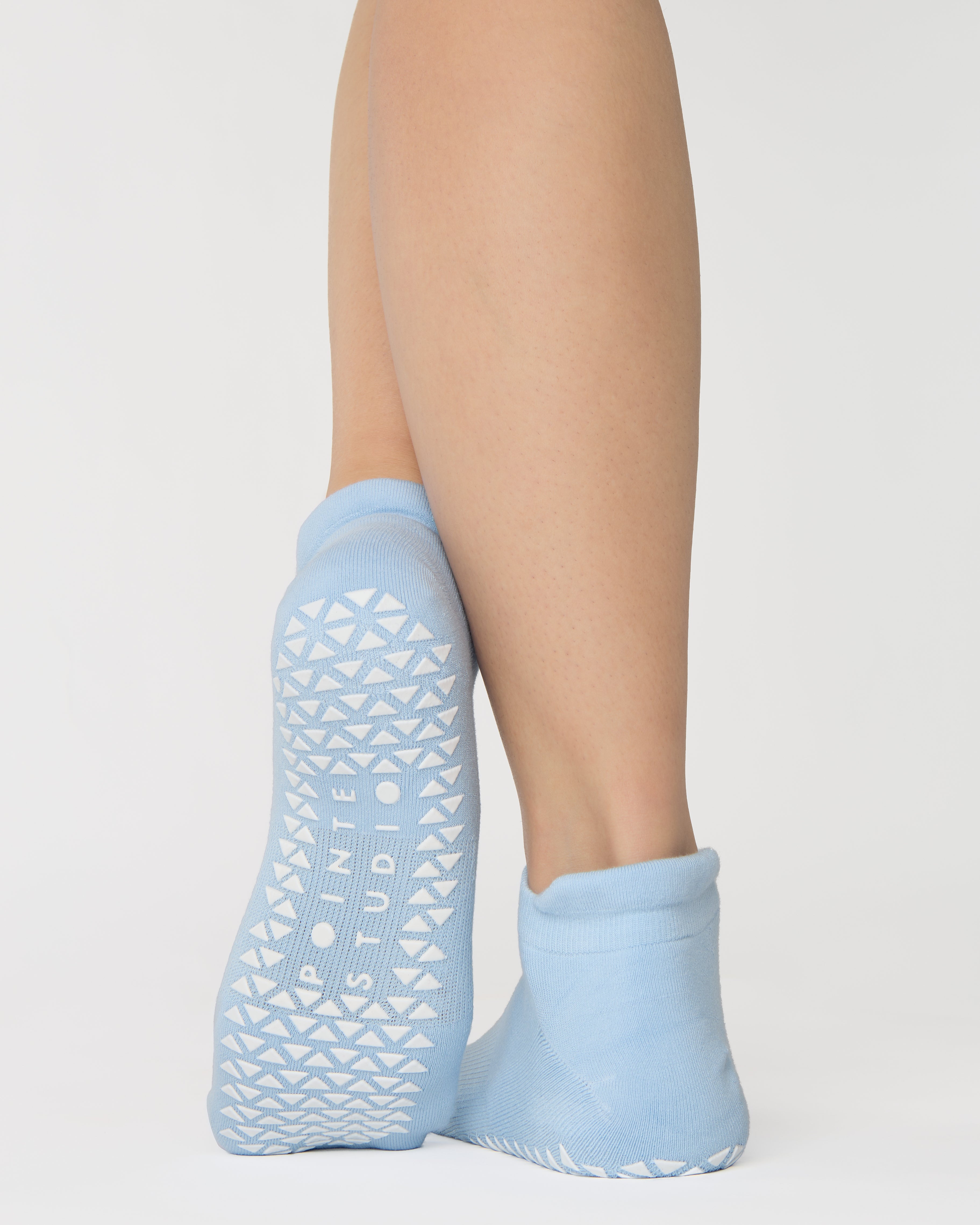 Women wearing a solid white full foot grip sock with a blue evil eye motiff on the top of the toes, made for pilates, barre, yoga, and beyond.