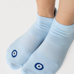 Women wearing a solid white full foot grip sock with a blue evil eye motiff on the top of the toes, made for pilates, barre, yoga, and beyond.