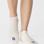 Women wearing a solid white full foot grip sock with a blue evil eye motiff on the top of the toes, made for pilates, barre, yoga, and beyond.
