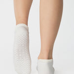 Women wearing a solid white full foot grip sock with a blue evil eye motiff on the top of the toes, made for pilates, barre, yoga, and beyond.