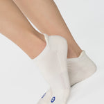 Women wearing a solid white full foot grip sock with a blue evil eye motiff on the top of the toes, made for pilates, barre, yoga, and beyond.